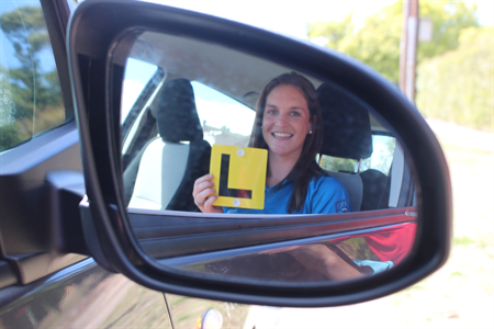 Image of side mirror on car showing a young woman with her L plates